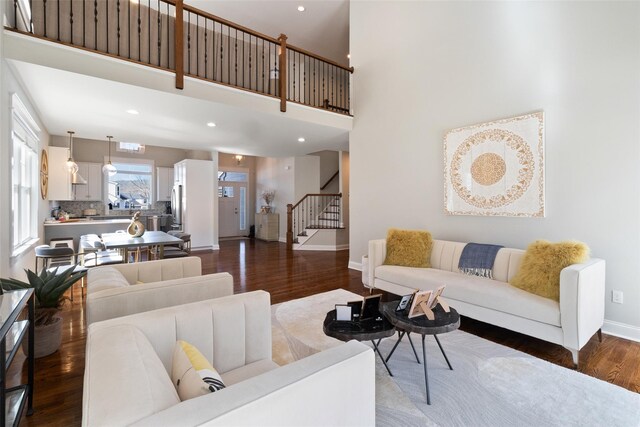 living area featuring dark wood-type flooring, baseboards, stairs, recessed lighting, and a high ceiling