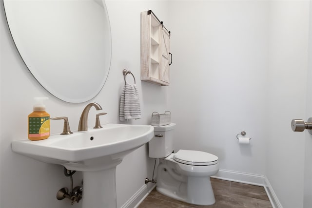 half bath with toilet, baseboards, and wood finished floors