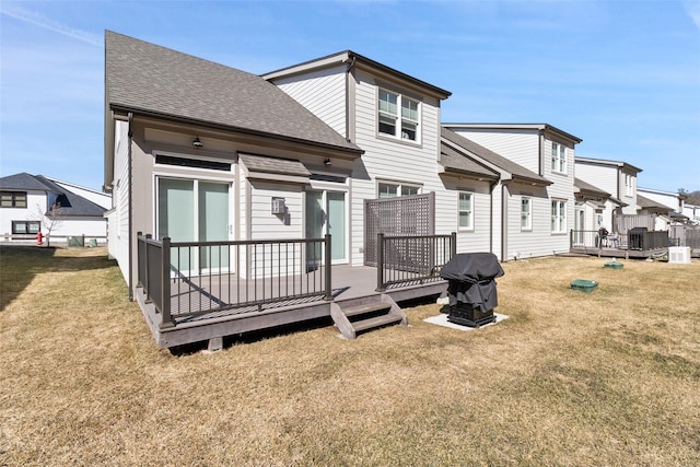 rear view of house with a wooden deck, a lawn, a shingled roof, and central AC