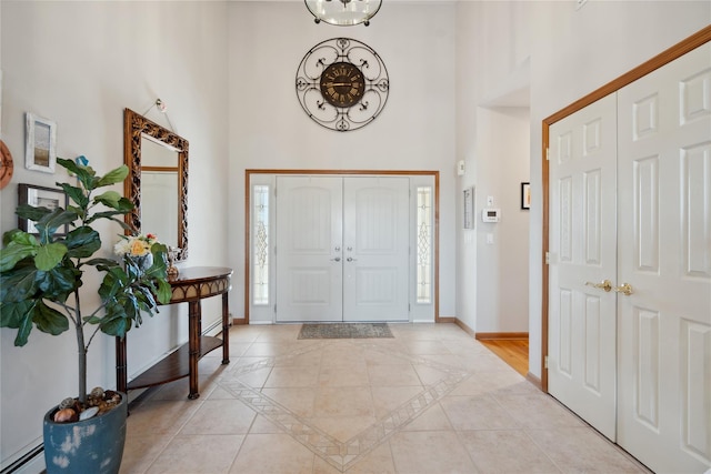 foyer entrance with light tile patterned floors, baseboard heating, baseboards, and a towering ceiling