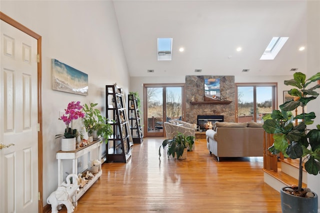 living room featuring visible vents, a stone fireplace, light wood-style flooring, a skylight, and high vaulted ceiling