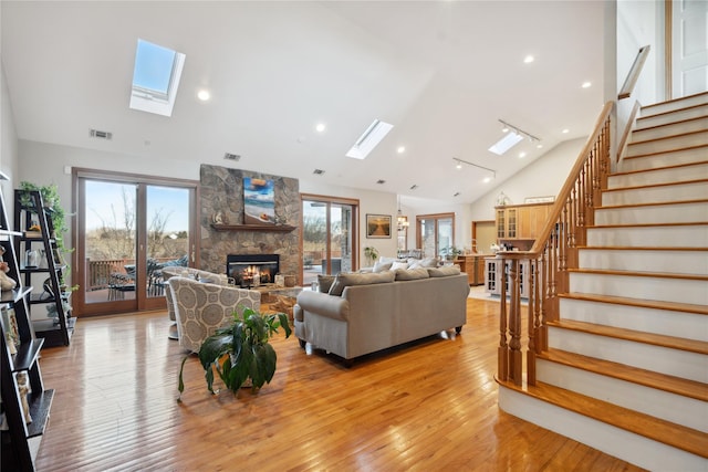 living area featuring visible vents, light wood finished floors, a skylight, a fireplace, and stairs