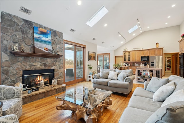 living area featuring light wood finished floors, visible vents, a fireplace, and a skylight