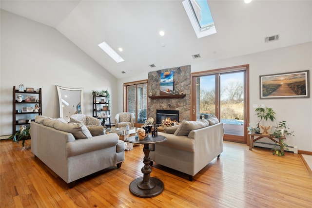 living area featuring baseboard heating, light wood-style flooring, a fireplace, a skylight, and high vaulted ceiling