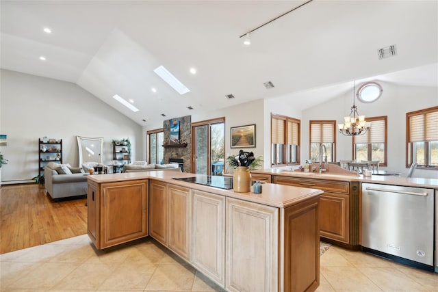 kitchen featuring visible vents, open floor plan, vaulted ceiling with skylight, a fireplace, and dishwasher