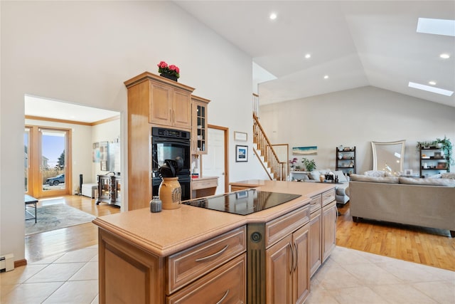 kitchen featuring black appliances, open floor plan, a center island, a skylight, and light tile patterned floors