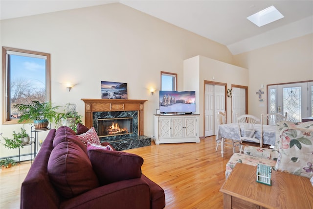 living room featuring a skylight, plenty of natural light, light wood-style floors, and a high end fireplace