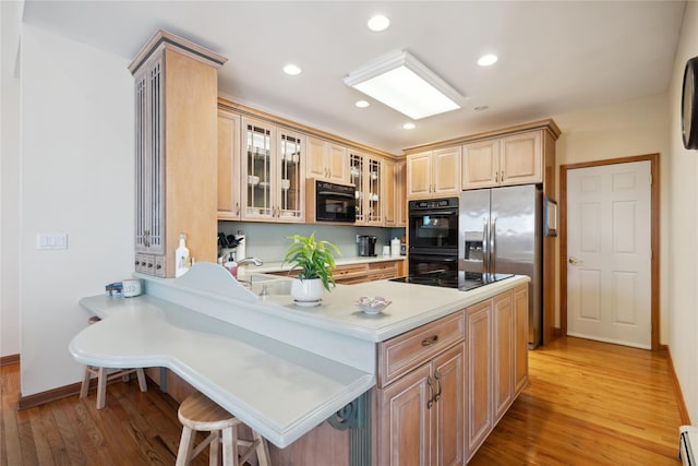 kitchen featuring light wood-type flooring, black appliances, a baseboard heating unit, a peninsula, and glass insert cabinets