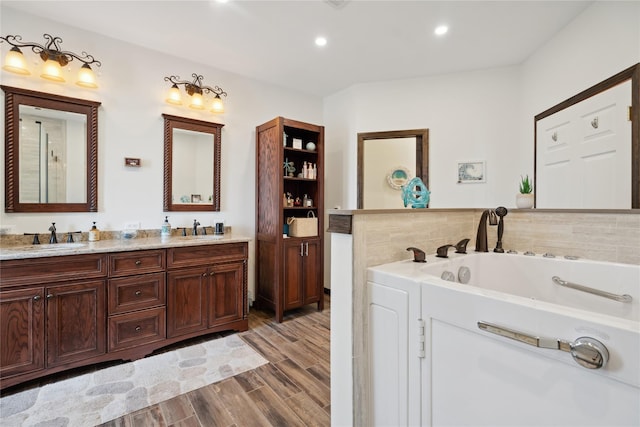 bathroom featuring double vanity, a garden tub, wood finished floors, and a sink