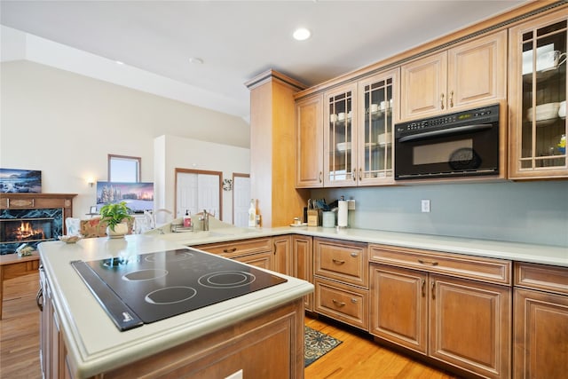 kitchen featuring light wood finished floors, a high end fireplace, light countertops, vaulted ceiling, and black appliances