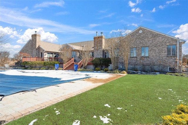 rear view of property featuring brick siding, a fenced in pool, a lawn, a deck, and a patio area