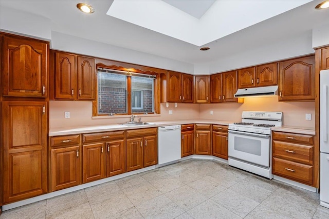 kitchen with under cabinet range hood, light countertops, brown cabinets, white appliances, and a sink