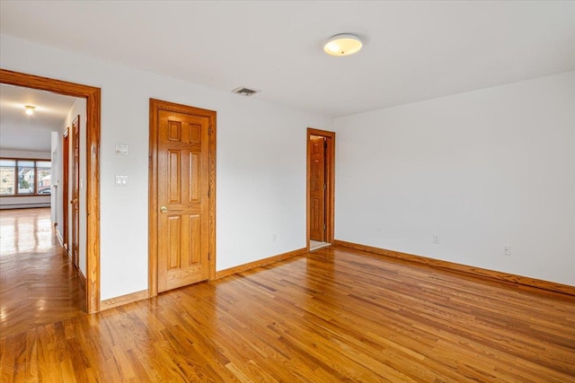 spare room featuring visible vents, baseboard heating, baseboards, and light wood-style floors