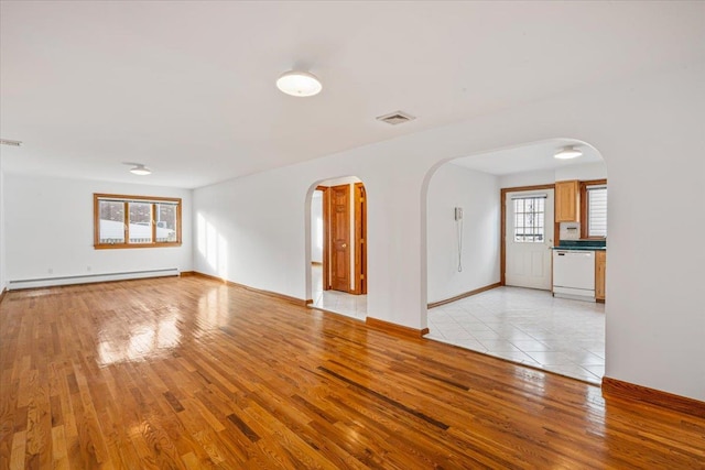 spare room featuring visible vents, arched walkways, baseboard heating, and light wood-style flooring