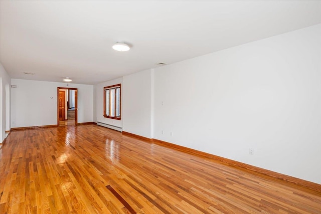 empty room with light wood-style flooring, a baseboard heating unit, and baseboards