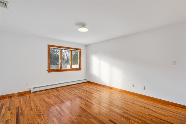 empty room featuring wood finished floors, visible vents, baseboard heating, and baseboards