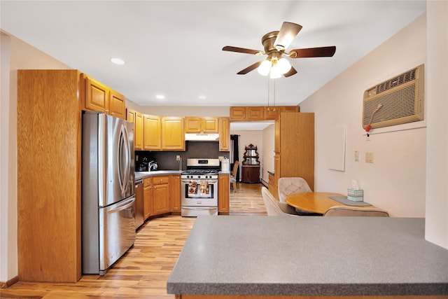 kitchen featuring a wall unit AC, a ceiling fan, light wood finished floors, under cabinet range hood, and appliances with stainless steel finishes