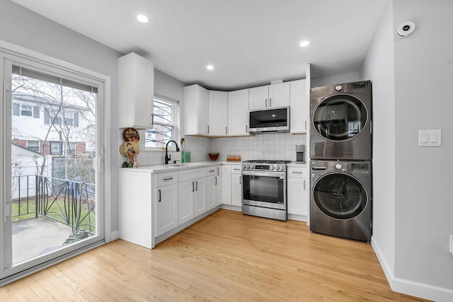 kitchen with stacked washer and clothes dryer, tasteful backsplash, appliances with stainless steel finishes, and light wood finished floors