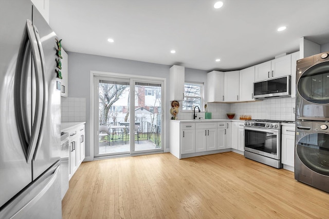 kitchen featuring light wood-style flooring, white cabinets, stainless steel appliances, and stacked washer / drying machine