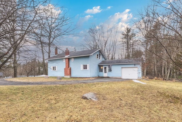 back of property with a lawn, driveway, a chimney, and an attached garage