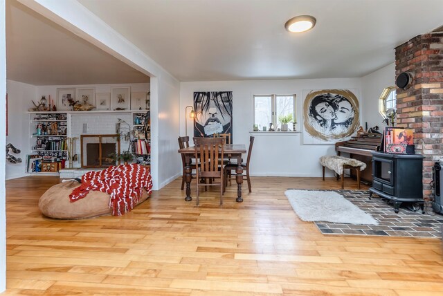 dining space with a fireplace, a wood stove, baseboards, and wood finished floors