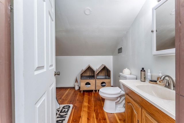 half bath with visible vents, toilet, wood finished floors, vanity, and vaulted ceiling