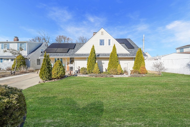 view of front of house with roof mounted solar panels, a chimney, and a front lawn