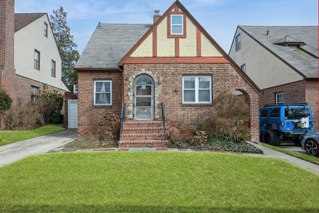 english style home with brick siding, a chimney, and a front yard