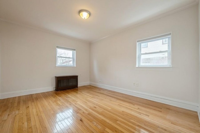 spare room with light wood finished floors, radiator heating unit, baseboards, and ornamental molding