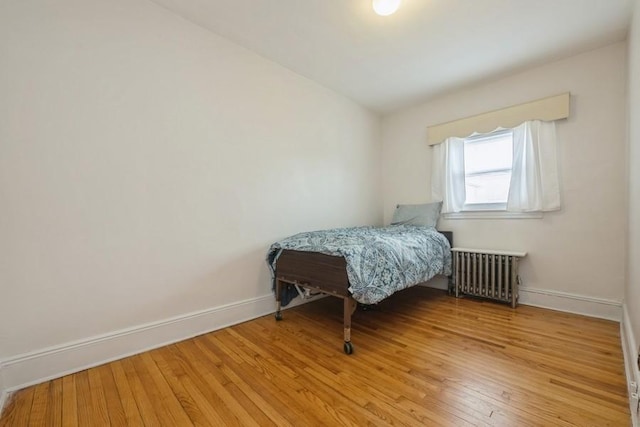 bedroom with radiator heating unit, baseboards, and light wood-type flooring