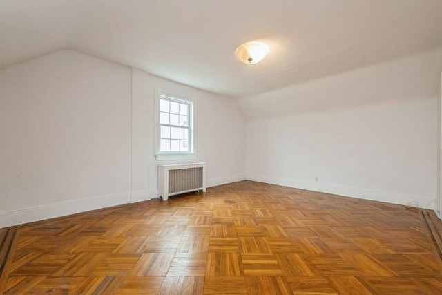 empty room with baseboards, radiator heating unit, and vaulted ceiling