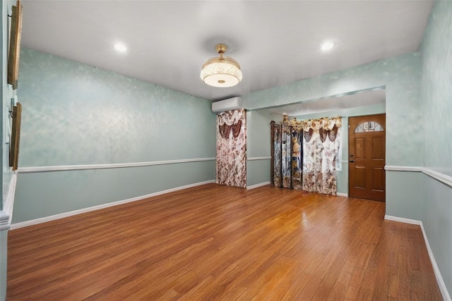 empty room featuring baseboards, a wall unit AC, and wood finished floors