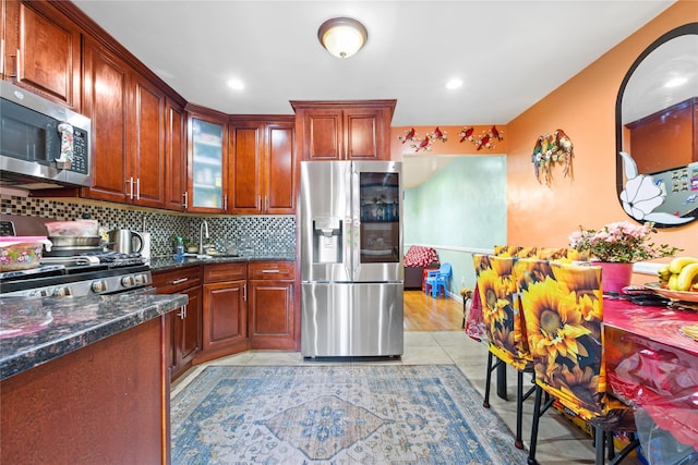 kitchen with light tile patterned floors, a sink, glass insert cabinets, appliances with stainless steel finishes, and backsplash