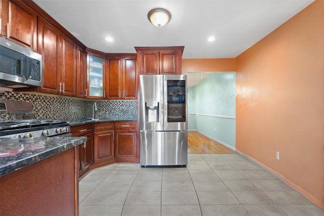 kitchen with light tile patterned floors, a sink, glass insert cabinets, appliances with stainless steel finishes, and tasteful backsplash