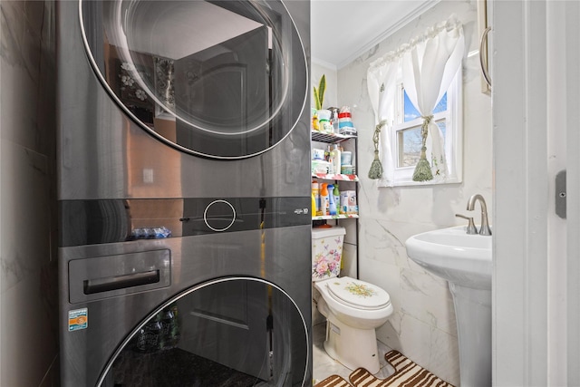 bathroom featuring toilet, tile walls, crown molding, and stacked washer / dryer