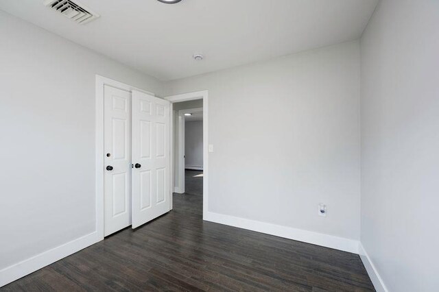 unfurnished bedroom featuring dark wood-style floors, visible vents, and baseboards