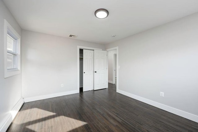 unfurnished bedroom with dark wood-type flooring, visible vents, baseboards, and a closet