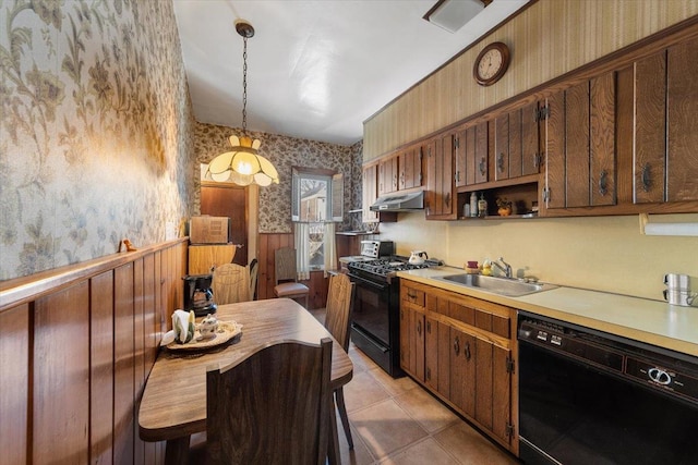 kitchen with black appliances, a sink, under cabinet range hood, wainscoting, and wallpapered walls