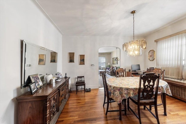 dining area featuring arched walkways, a chandelier, baseboards, and wood finished floors