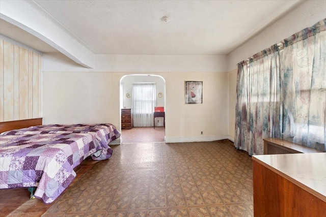 bedroom featuring tile patterned floors, baseboards, arched walkways, and a textured ceiling