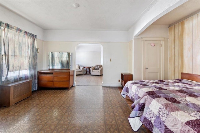 bedroom with arched walkways, radiator, and a textured ceiling