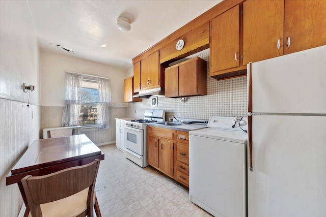 kitchen with under cabinet range hood, light floors, brown cabinetry, white appliances, and washer / clothes dryer