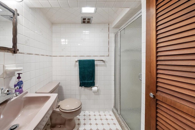 bathroom featuring a sink, toilet, tile walls, and a shower stall