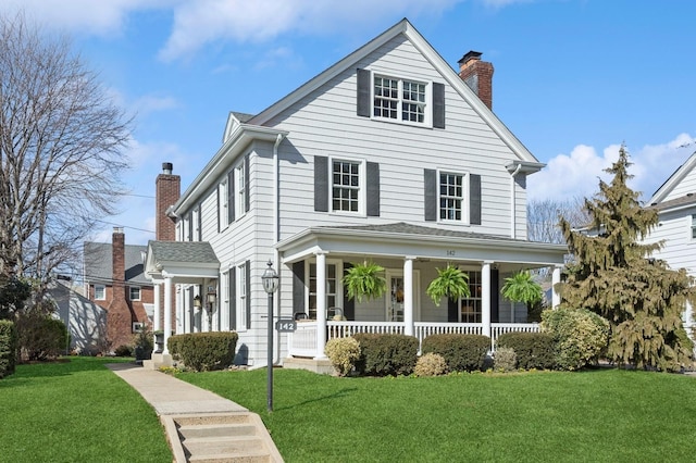 view of front of home featuring a chimney, covered porch, and a front lawn