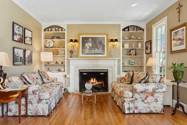 sitting room featuring ornamental molding, a fireplace, built in shelves, and wood-type flooring