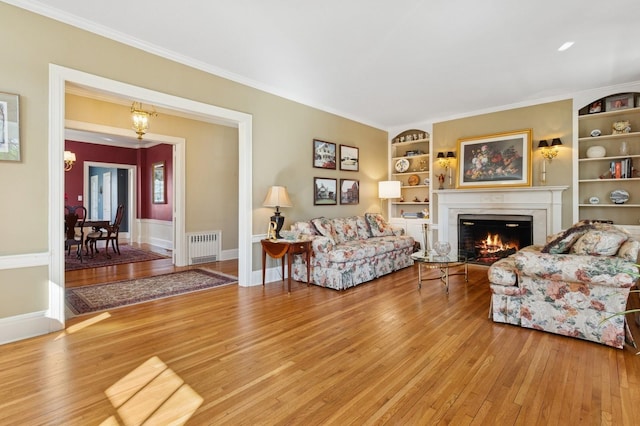 living room featuring a warm lit fireplace, radiator heating unit, light wood-style floors, and ornamental molding