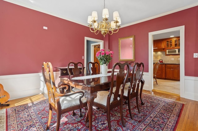 dining area with a wainscoted wall, light wood-style flooring, crown molding, and an inviting chandelier