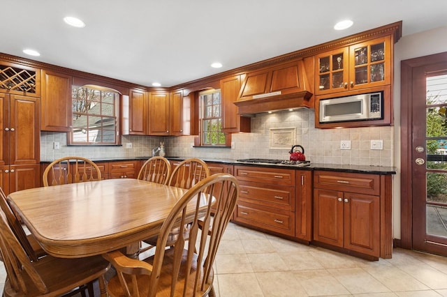 kitchen with light tile patterned floors, brown cabinetry, glass insert cabinets, appliances with stainless steel finishes, and backsplash