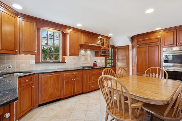 kitchen with custom exhaust hood, a sink, decorative backsplash, appliances with stainless steel finishes, and brown cabinets