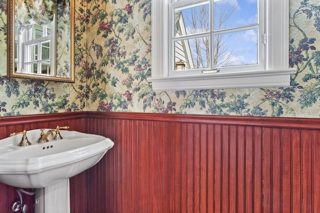 bathroom featuring wallpapered walls, a sink, and wainscoting